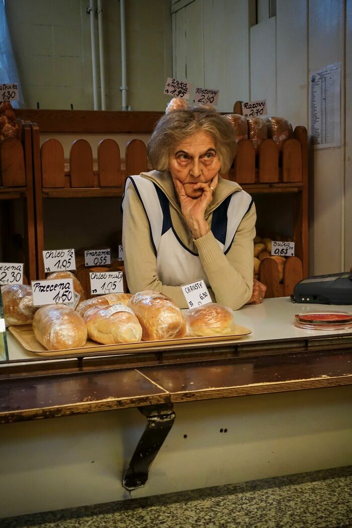 An elderly woman with a pensive expression behind a counter, evoking deeply evil feelings.