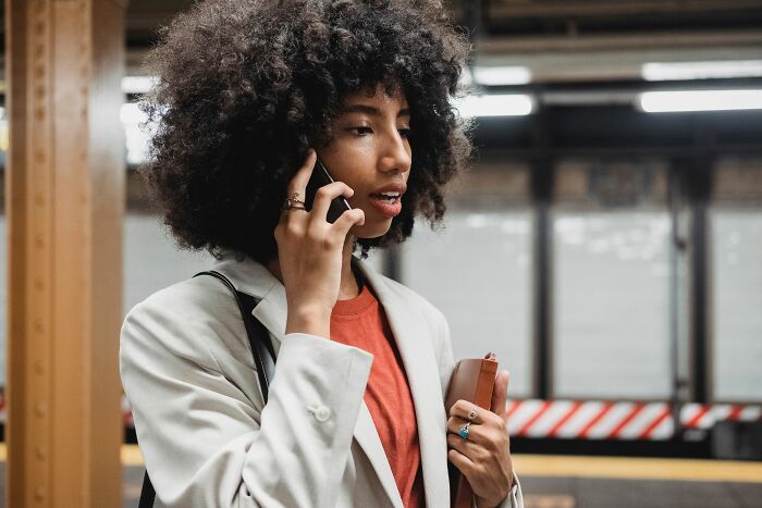 Woman with curly hair on a subway platform talking on her phone, illustrating a scenario for pocket dial stories.