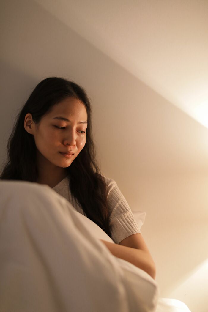 A sad woman in bed, holding a pillow, possibly feeling the impact of cheating red flags.