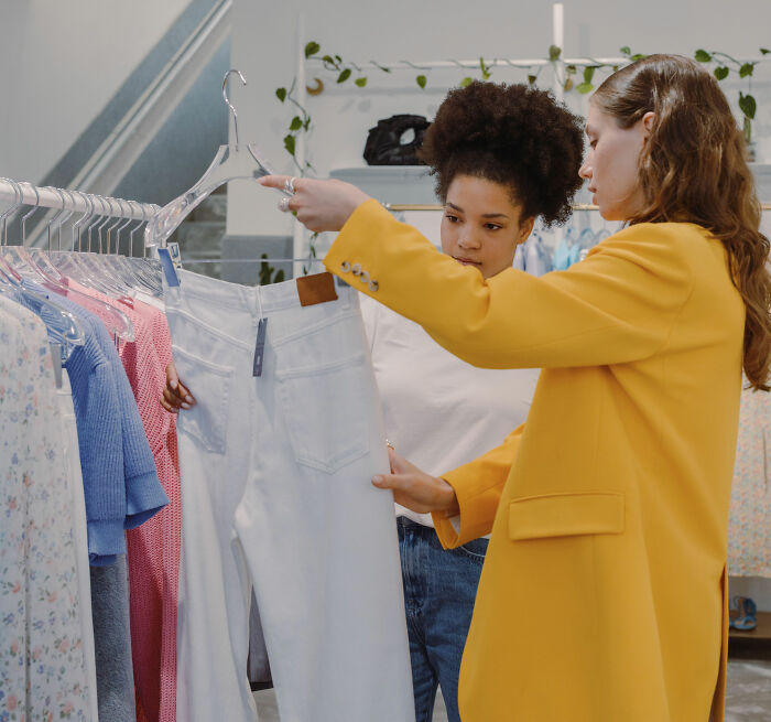 Two women browsing clothing selection at a store, discussing a pair of white jeans. Plus-size influencer clothing options. Two women browsing clothing selection at a store, discussing a pair of white jeans. Plus-size influencer clothing options.