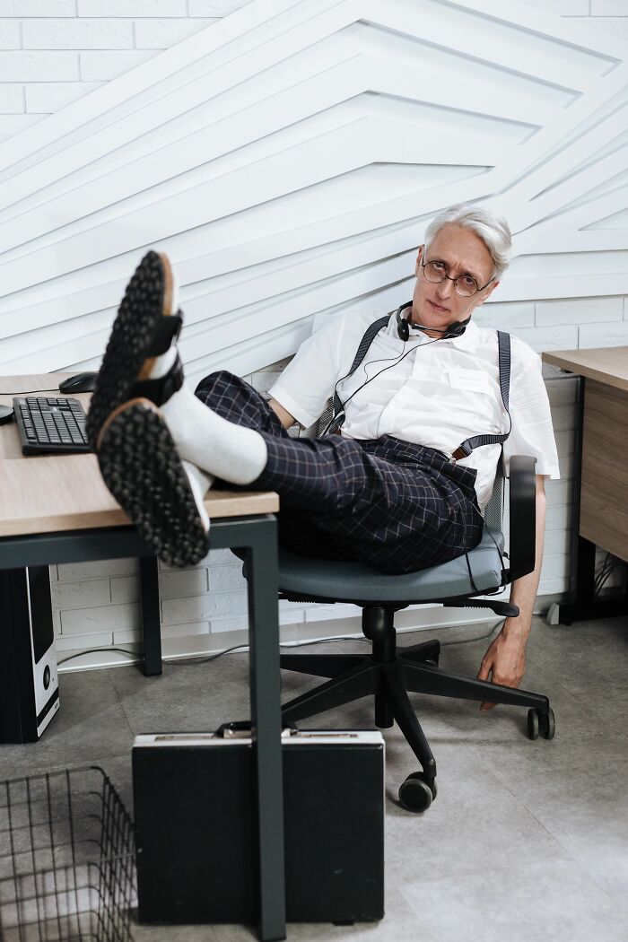 A man with gray hair and glasses, wearing suspenders, with his feet on a desk, representing a final day at work.