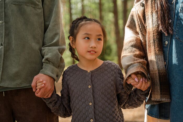 A young girl holds hands with her parents in a forest, representing the experiences of parents terrified of their children.