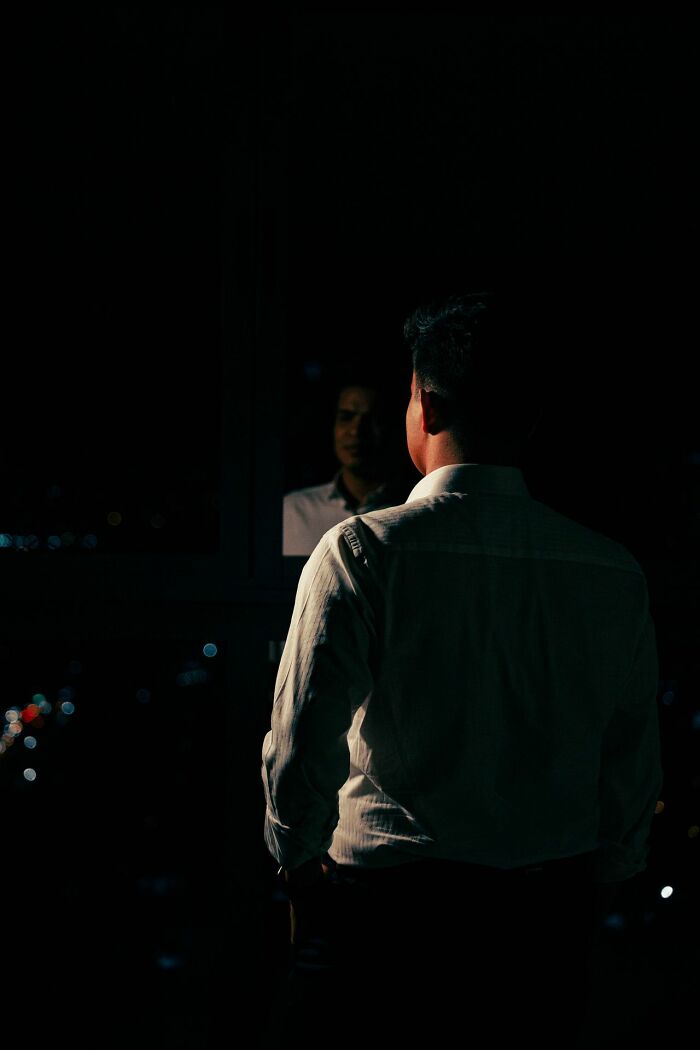A man's silhouette in a dark room, reflecting deeply evil encounters.