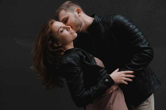 A man embraces and kisses a woman on the cheek, both dressed in leather jackets. This image relates to secrets and how they could do damage.