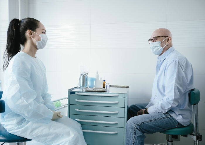 Doctor and patient, both masked, discuss pneumonia warning signs in a clinical setting. Doctor and patient, both masked, discuss pneumonia warning signs in a clinical setting.