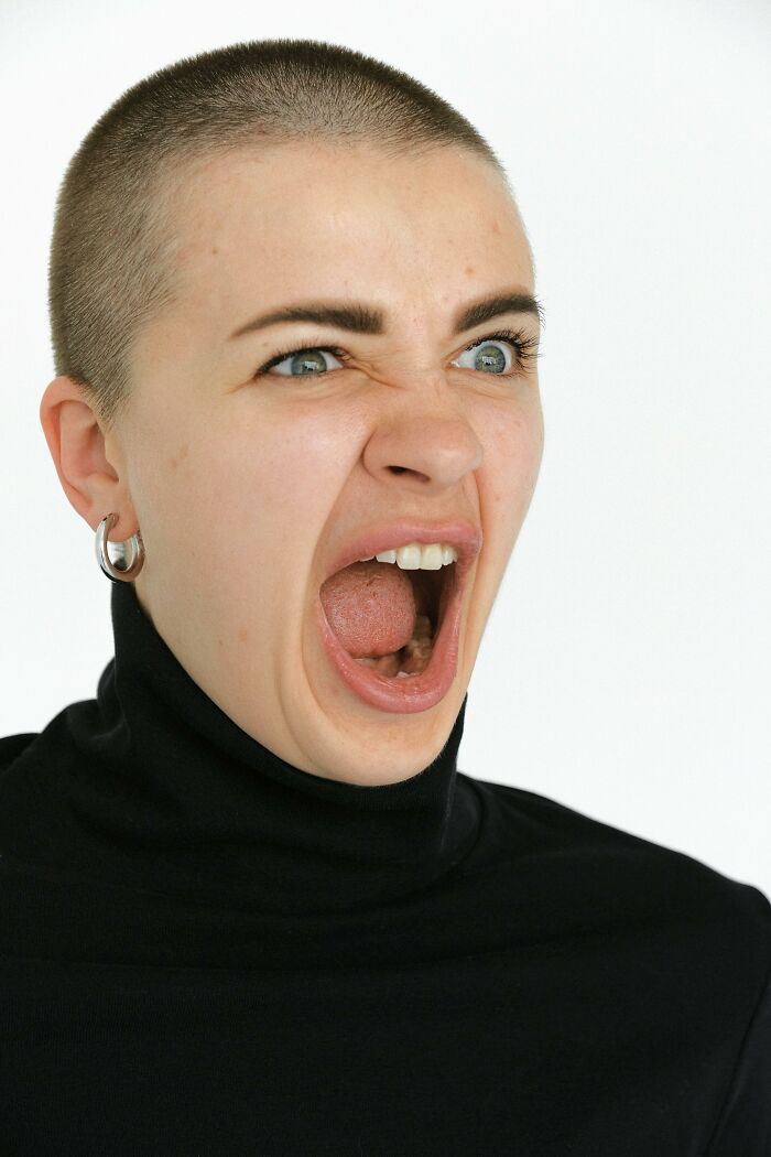 A woman with a shaved head and black turtleneck screams, demonstrating how people handle stress. A woman with a shaved head and black turtleneck screams, demonstrating how people handle stress.