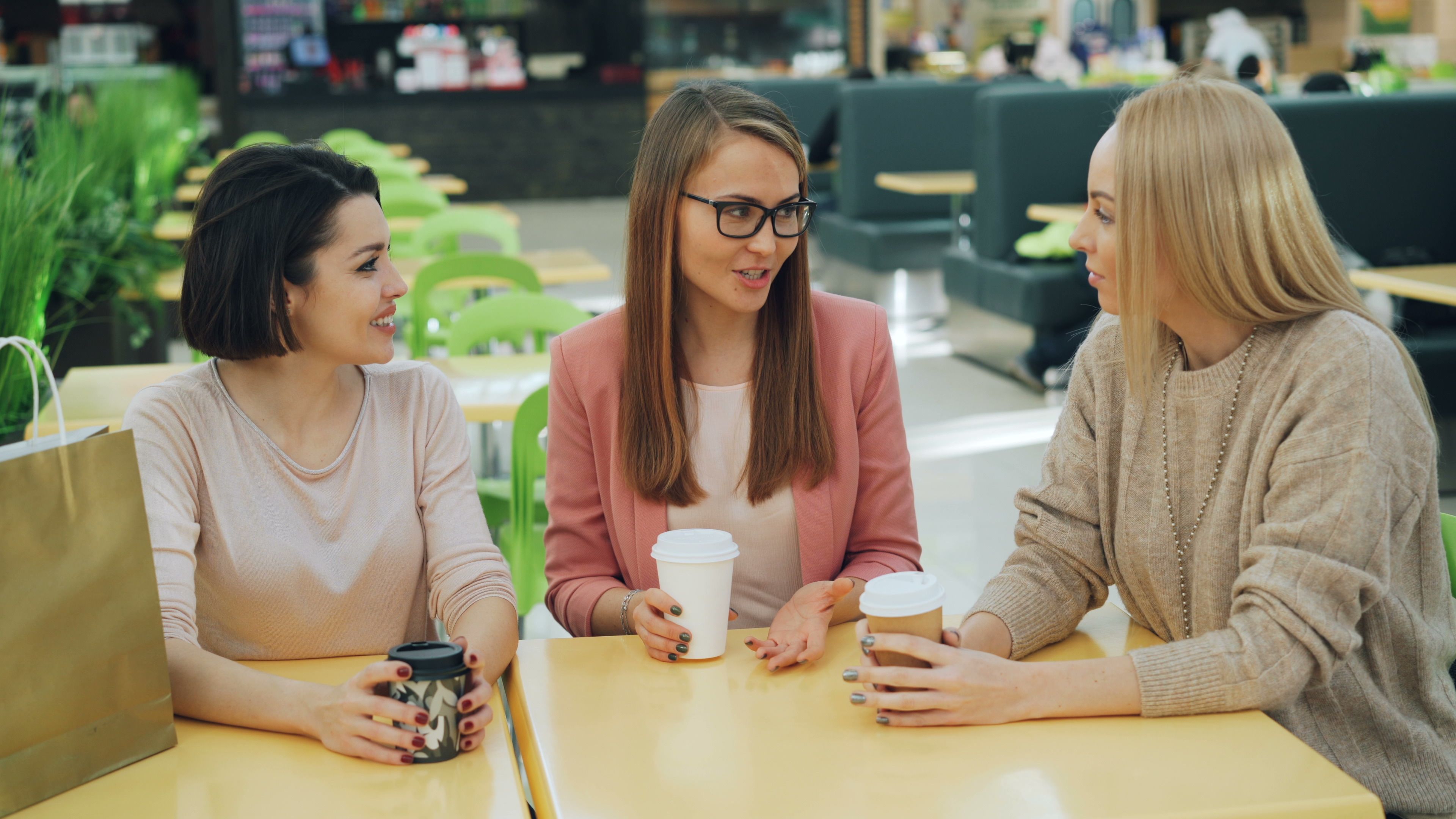 Three women gossiping while holding coffee cups in a cafe, a visual representation of spilling the tea.