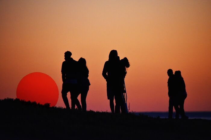 Silhouetted people on a hill watching a large, red total solar eclipse, suggesting popular viewing spots. Silhouetted people on a hill watching a large, red total solar eclipse, suggesting popular viewing spots.