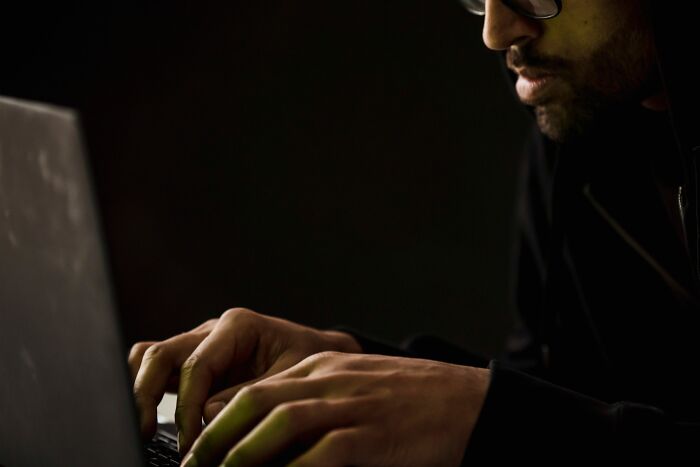 Man with glasses typing on a laptop in a dark room, illustrating industry secrets of cybersecurity jobs.