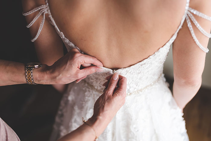 Close-up of hands fastening bride's white lace wedding dress with beaded straps Close-up of hands fastening bride's white lace wedding dress with beaded straps