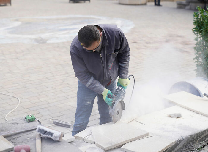 Landscaper using an angle grinder, making cuts on stone tiles for a patio installation project, getting his revenge. Landscaper using an angle grinder, making cuts on stone tiles for a patio installation project, getting his revenge.