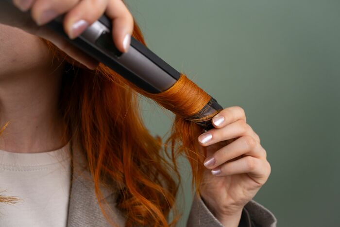A person styling their red hair with a hair straightener, representing shocking ways people have lost their lives.