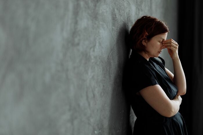 A woman leaning against a wall, looking distressed, symbolizing infuriating MILs stories.