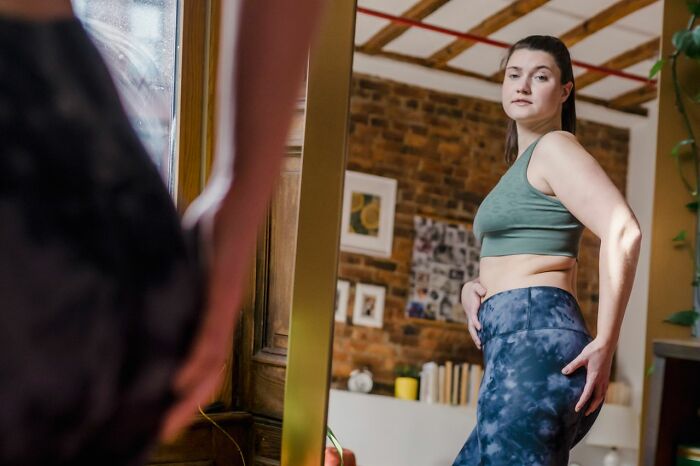 A woman looking at herself in a mirror, adjusting her workout pants. This image reflects unhinged therapist moments.