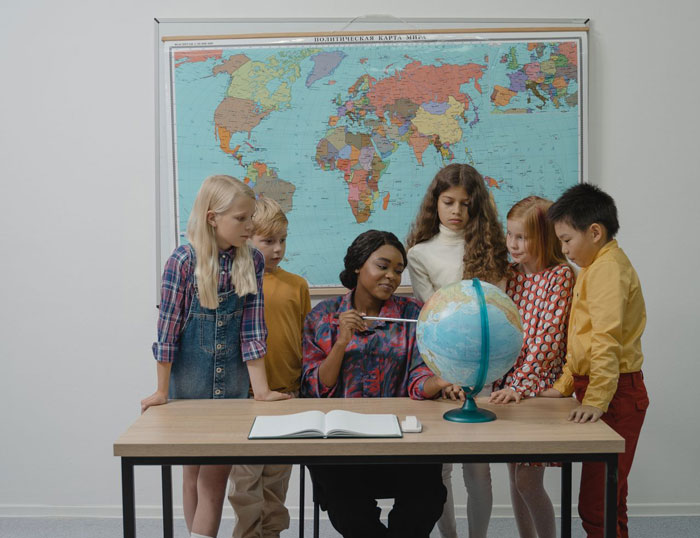 A woman shows students the actual scale of continents on a globe, highlighting the true scale of continents.