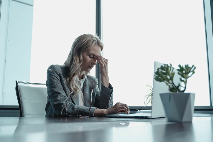 A woman at a desk with a laptop, hand to her forehead, frustrated by entitled friends.