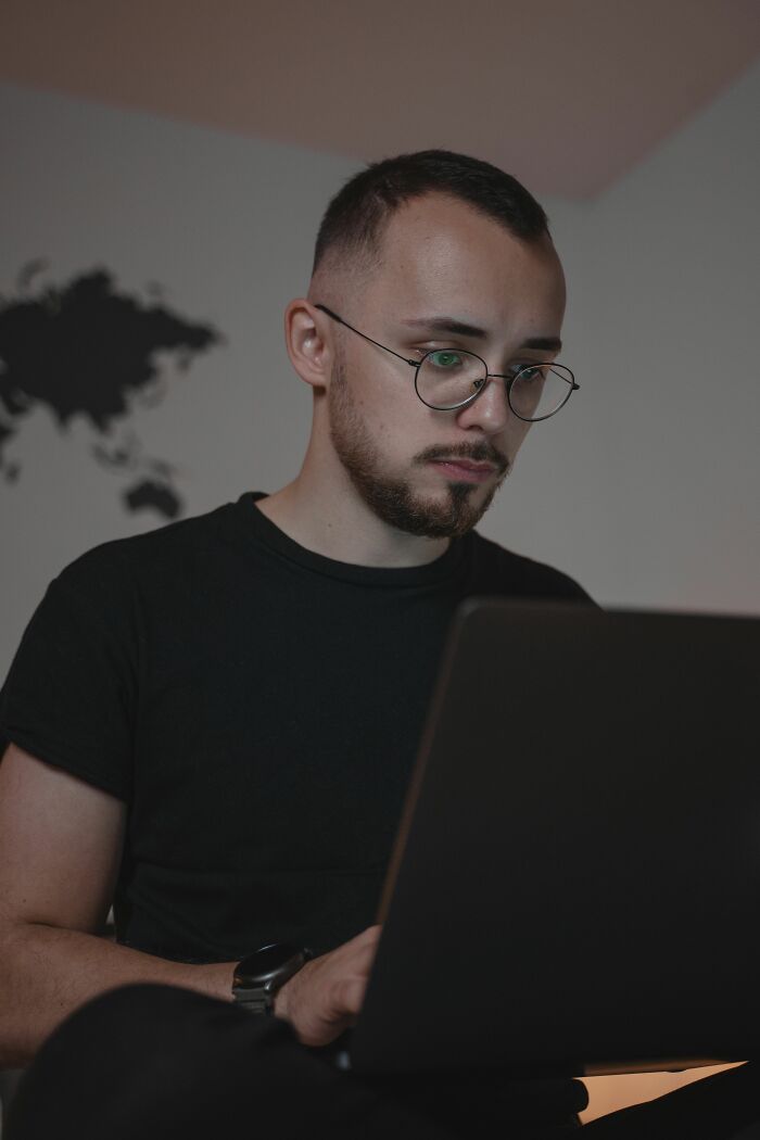 Man wearing glasses intently working on his laptop, revealing industry secrets about his job.