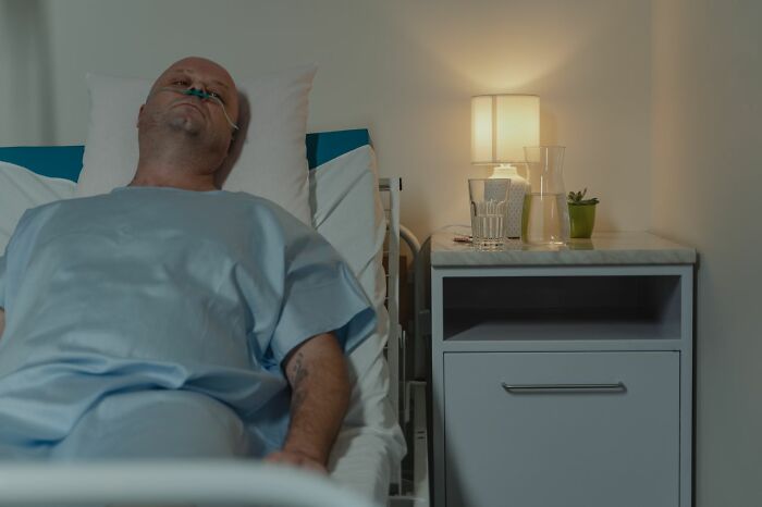 A man with a nasal cannula lies in a hospital bed, looking at the ceiling, depicting unusual ways people lost their lives.