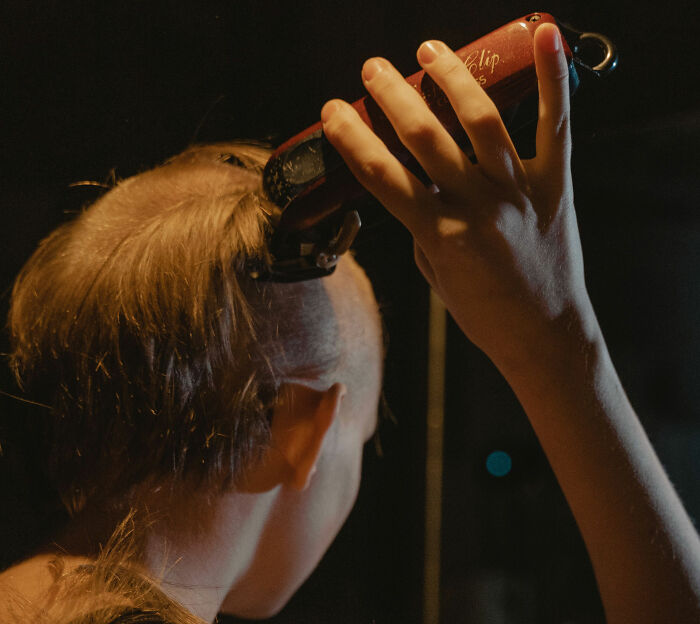 Close-up of a person's hand using an electric shaver to shave hair, relating to daughter's hair being shaved. Close-up of a person's hand using an electric shaver to shave hair, relating to daughter's hair being shaved.