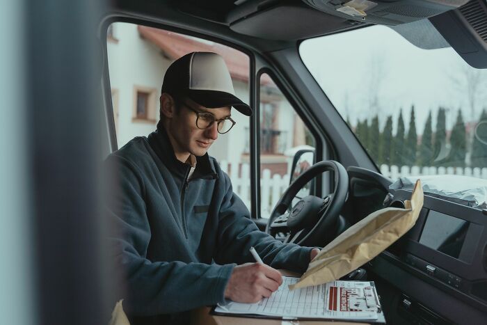A delivery driver signing a document inside his van, an example of a dumb reason people got fired.