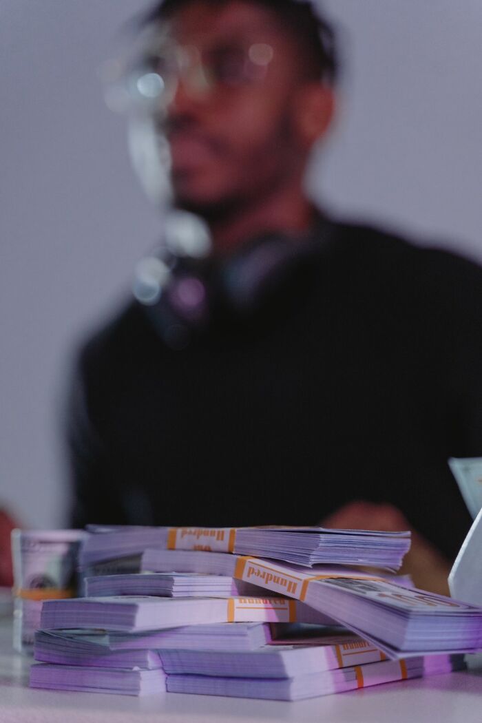 Stacks of money on a table with a person in the background, hinting at financial secrets.