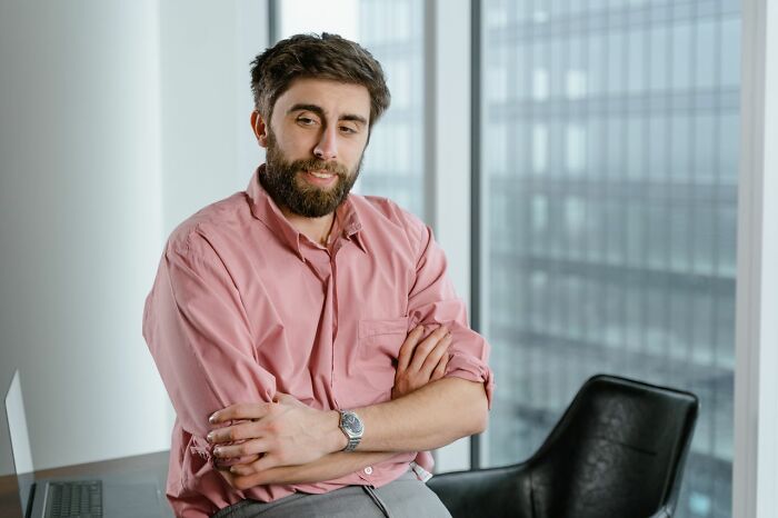 A bearded man in a pink shirt with crossed arms, looking like people's instincts tell them to get away from creeps.