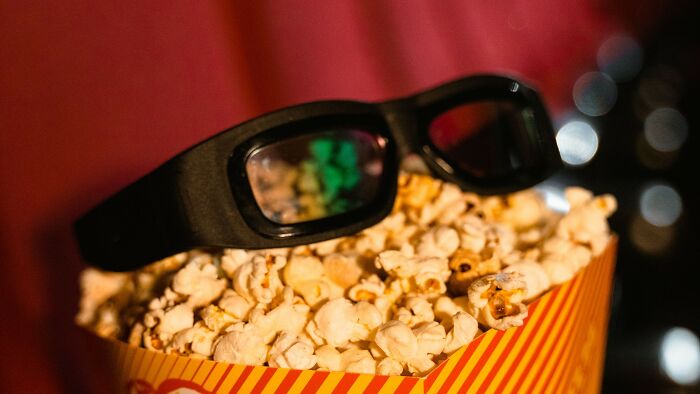 A close-up of a container of popcorn with 3D movie glasses resting on top, inviting viewers to solve movie puzzles.