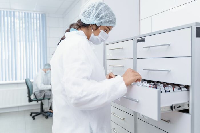 A scientist in a lab coat and mask, examining files in a cabinet, hinting at company secrets.