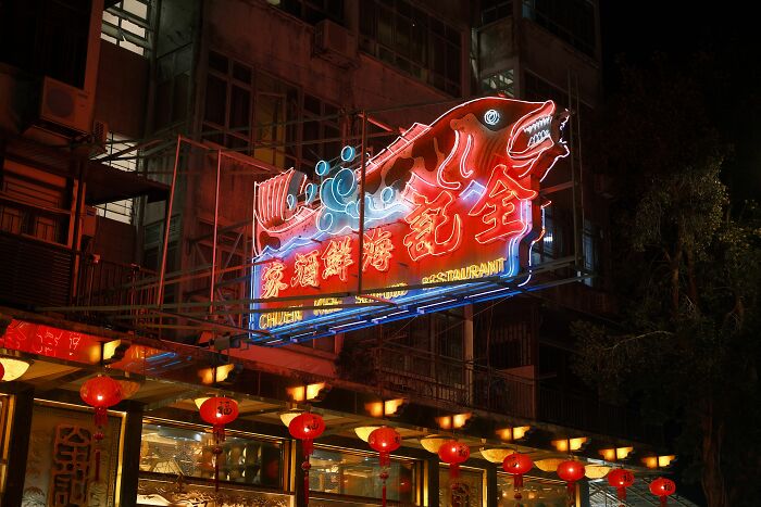 A vibrant neon fish sign outside a restaurant at night, indicating health inspections failures.