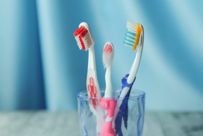 Three toothbrushes in a clear glass, showing different versions of normal at a friend's house.
