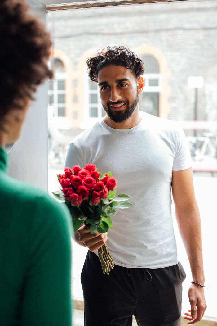 A man holding a bouquet of red roses, smiling at a woman, symbolizing love before getting married.