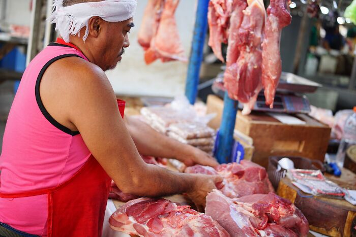 A man in a pink tank top and red apron preparing meat at a market, related to shocking health inspections failures.