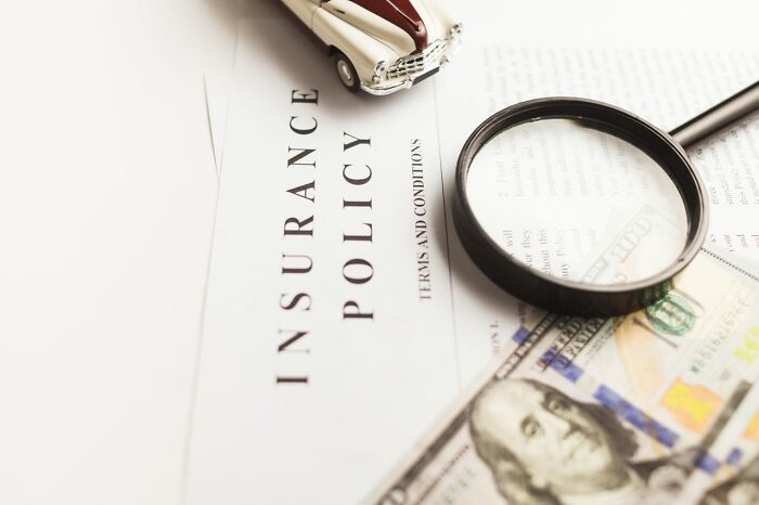 Insurance policy document with a magnifying glass, car, and cash, illustrating companies behind the scenes secrets.