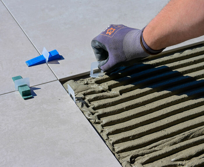 A hand in a glove setting tiles, showcasing precise tile work. Focus on landscaper revenge. A hand in a glove setting tiles, showcasing precise tile work. Focus on landscaper revenge.