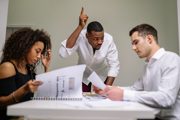 A man with raised finger, appearing to debate with colleagues, highlighting psychological red flags in workplace communication.