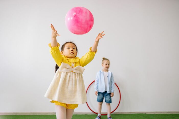 A young girl in a yellow dress reaching for a pink ball, symbolizing the rarest things that have happened.