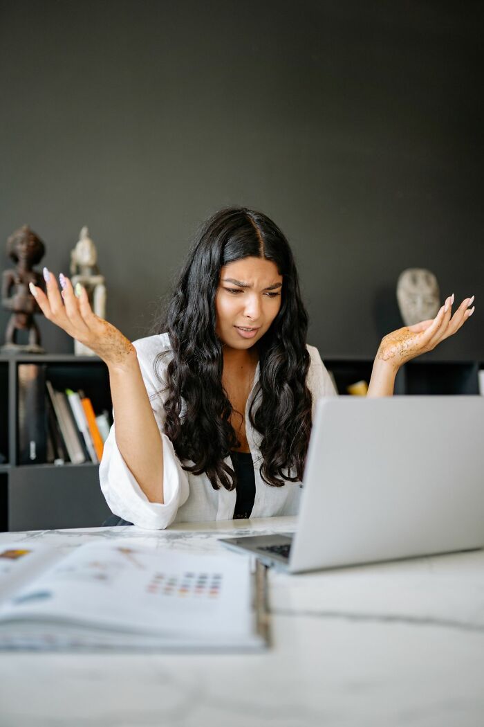 A woman at a laptop shrugging in confusion, illustrating the bewilderment caused by entitled friends.