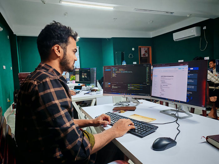 A man working as an IT guy at a desk with multiple monitors, coding and reviewing documents for greedy bosses. A man working as an IT guy at a desk with multiple monitors, coding and reviewing documents for greedy bosses.
