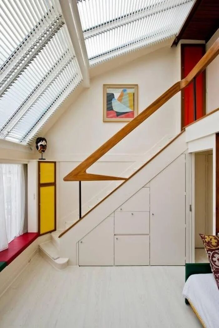 A modern Historic Interiors design featuring a bright room with skylights, a white staircase with wooden railing, and a colorful abstract painting.