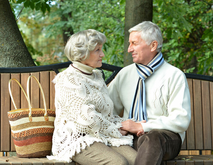 A senior couple sitting on a park bench, sharing World War II veterans' extraordinary stories.