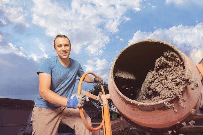 A smiling man operates a cement mixer, illustrating construction industries that make millions.