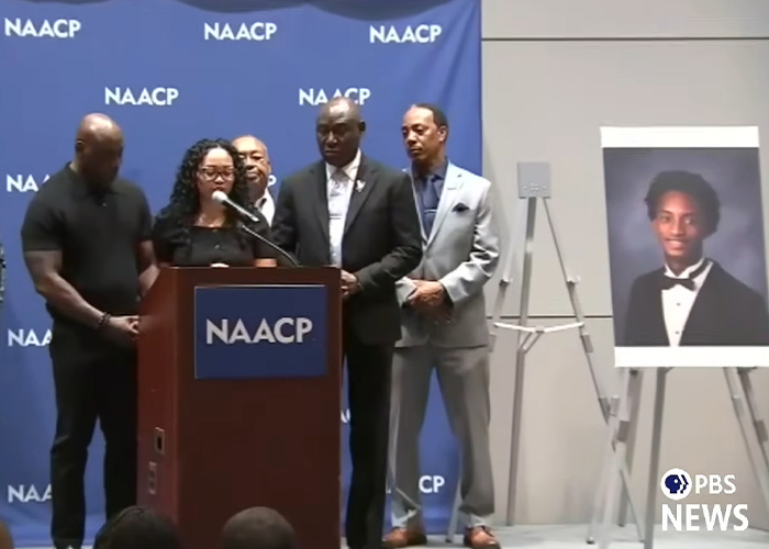 A group of people at a podium with an NAACP banner and a portrait of Nolan Wells. Preliminary autopsy results were released.