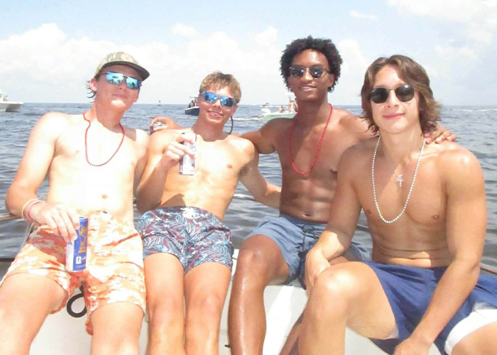 Four young men smiling on a boat. Preliminary autopsy results for the Nolan Wells case raise questions.
