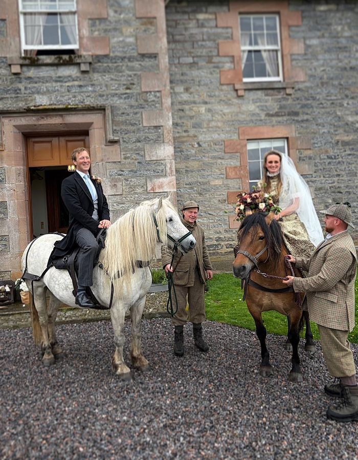 A newlywed couple on horseback outside a grand estate at their fairytale wedding. A newlywed couple on horseback outside a grand estate at their fairytale wedding.