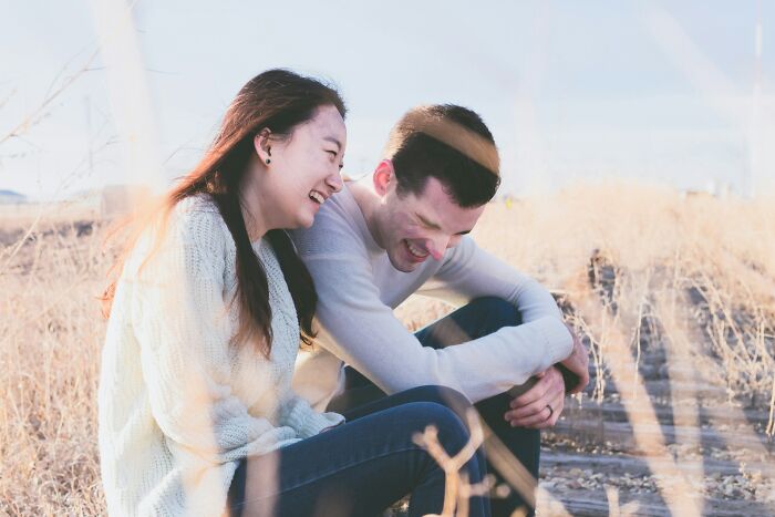 A couple laughs together in a field, showing subtle signs someone isn't as nice as they pretend to be.