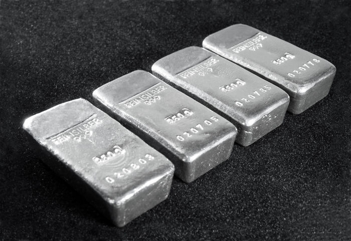 Four silver bars with inscriptions like Feinsilber 999 are neatly arranged on a dark surface, symbolizing history.