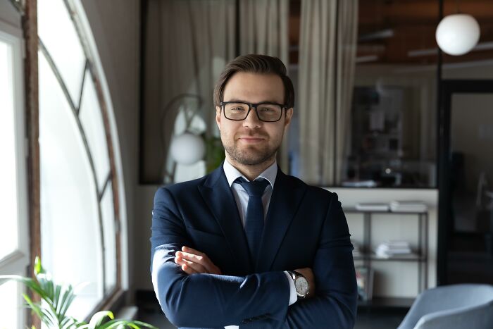 A confident man in a suit and glasses, illustrating jobs guys have that make women swipe left.