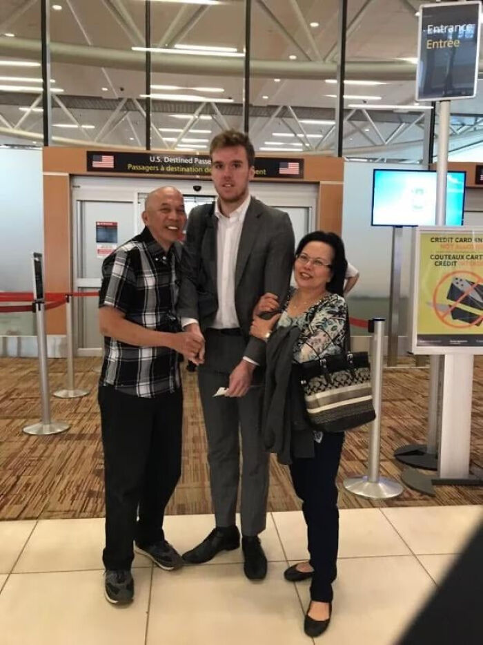 A tall man in a suit posing for a photo with two older people at an airport, highlighting moments people asked celebrities for a photo.