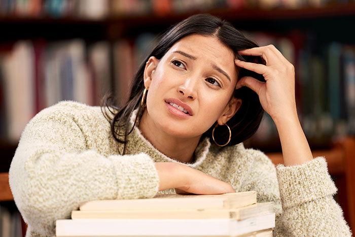 A mixed-race mom looks exasperated, resting her head on books, tired of explaining her blue-eyed kid. A mixed-race mom looks exasperated, resting her head on books, tired of explaining her blue-eyed kid.