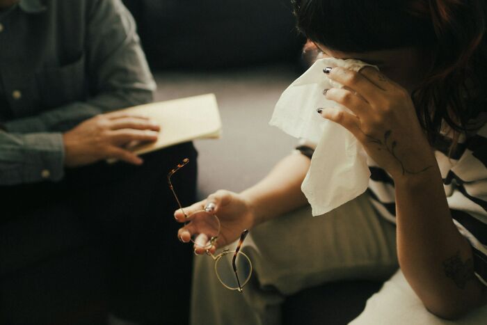 A person crying and holding a tissue during a therapy session, highlighting unhinged therapist moments and the need for a therapist.